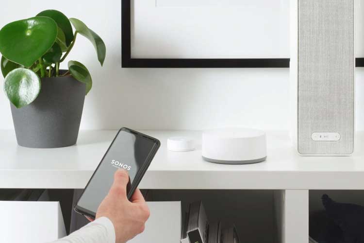 IKEA Symfonisk via Sprachbefehl steuern: Hand mit Handy und Sonos App, im Hintergrund ein Symfonisk Lautsprecher